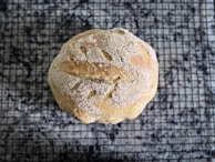 Close-up of a warm, golden-brown homemade bread loaf cooling on a kitchen towel.