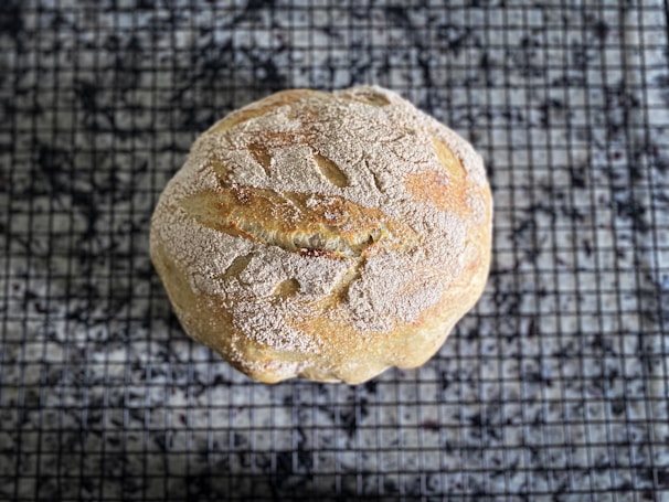 A warm loaf of artisan bread cooling on a kitchen counter dusted with flour.