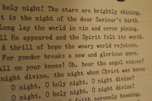 Typed text on a textured paper background featuring lines from the Christmas carol 'O Holy Night'. The text appears to be typed with an old-fashioned typewriter font, and the paper has a warm, sepia tone.