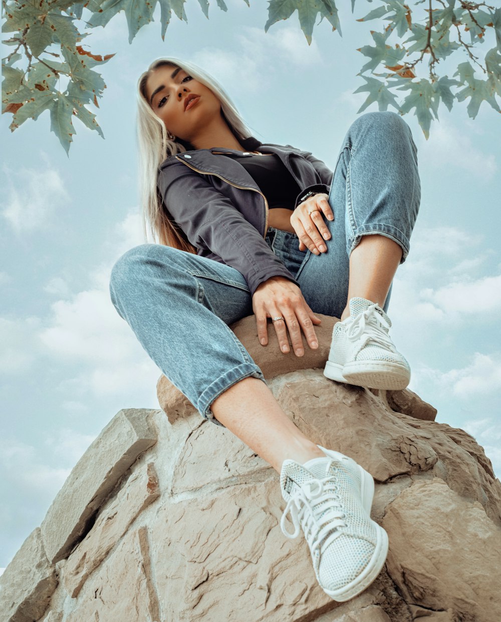 a woman sitting on top of a rock next to a tree