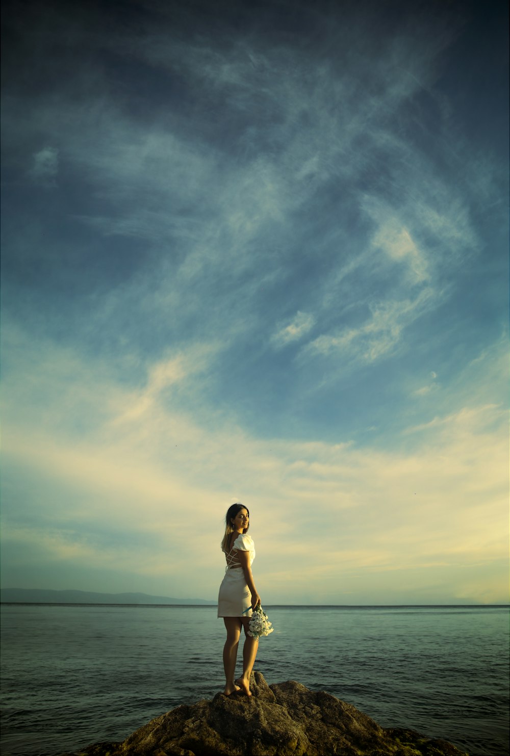 a woman standing on top of a rock near the ocean