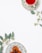 A cup of red herbal tea sits on an ornate plate with a floral pattern, placed alongside green eucalyptus leaves. A second decorative plate holds dried fruit, also adorned with eucalyptus sprigs, arranged on a clean, white surface.