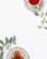 A cup of red herbal tea sits on an ornate plate with a floral pattern, placed alongside green eucalyptus leaves. A second decorative plate holds dried fruit, also adorned with eucalyptus sprigs, arranged on a clean, white surface.