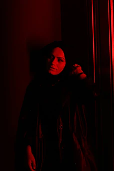 A shadowy figure standing under dim red light, evoking mystery and dark passion.