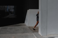 Model walking through a dimly lit alley wearing oversized jacket with gold zippers, city lights blurred behind.