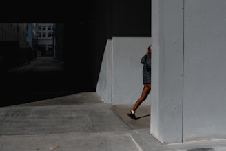 Model walking through a dimly lit alley wearing oversized jacket with gold zippers, city lights blurred behind.