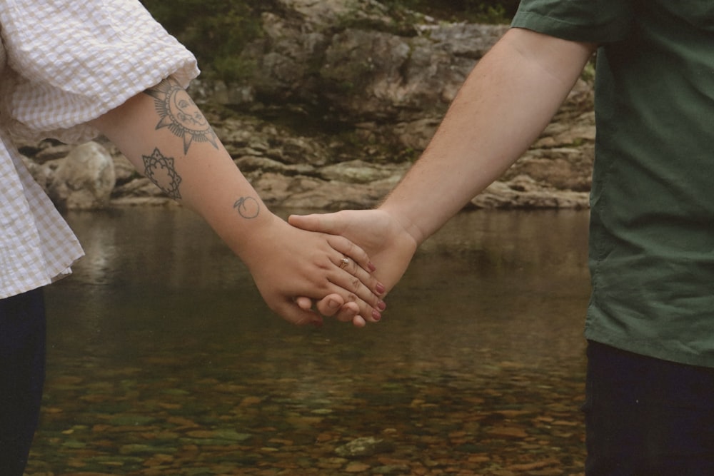 two people holding hands over a body of water