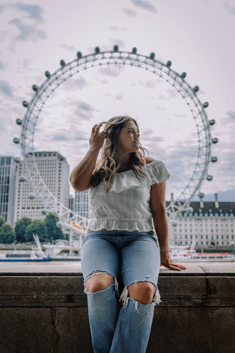 a woman sitting on a ledge in front of a ferris wheel