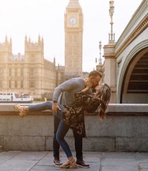 a man and woman kissing in front of a clock tower