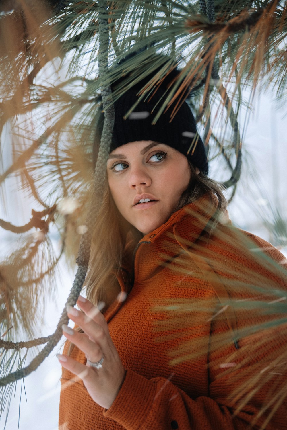 a woman in an orange coat holding a pine tree