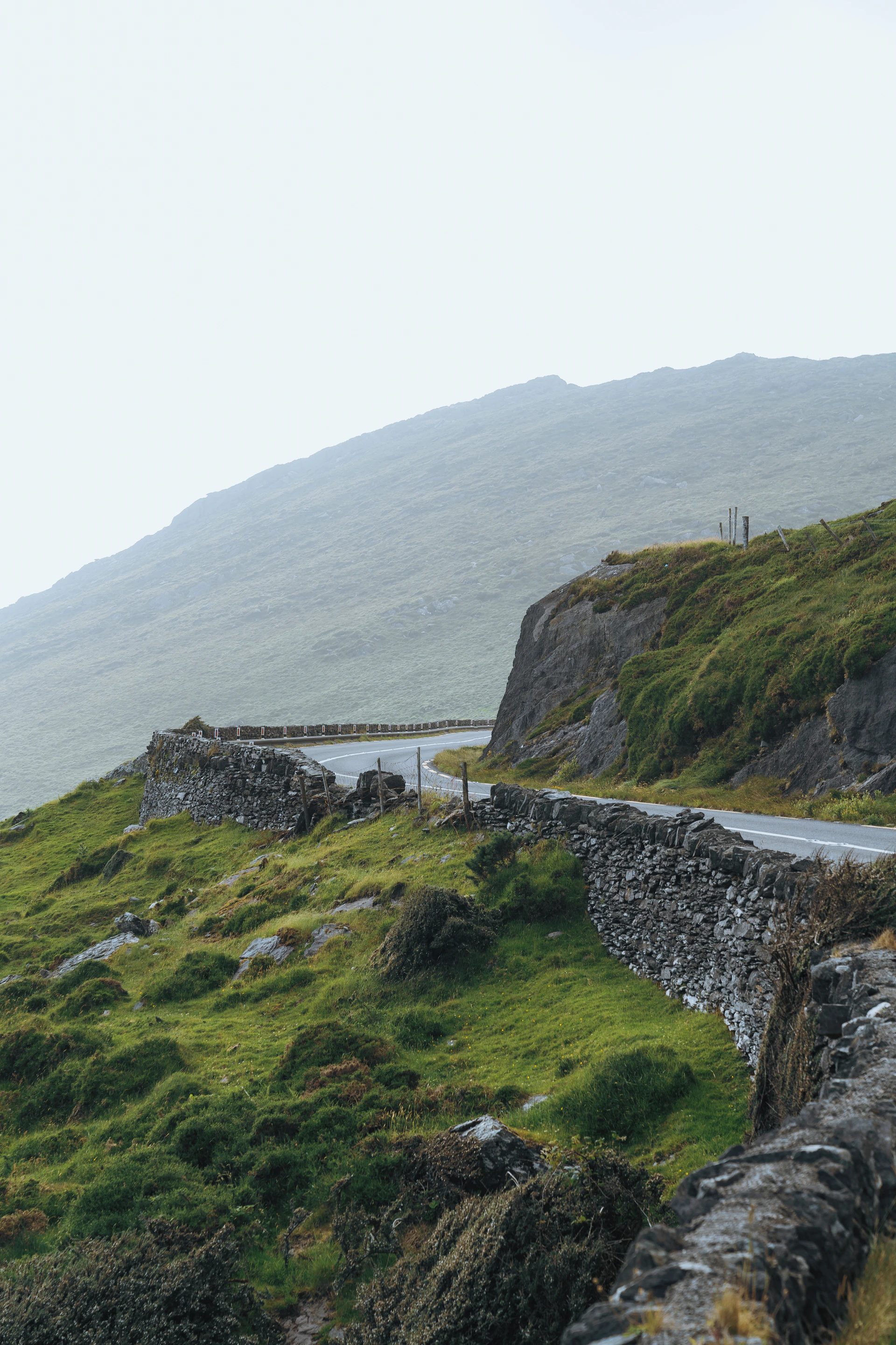 A misty morning view of Ireland's lush green hills dotted with ancient stone cottages and winding country roads.