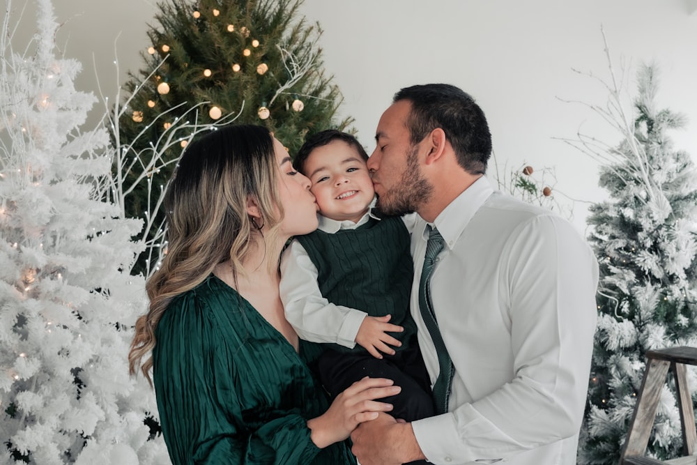 a man and woman kissing a child in front of a christmas tree