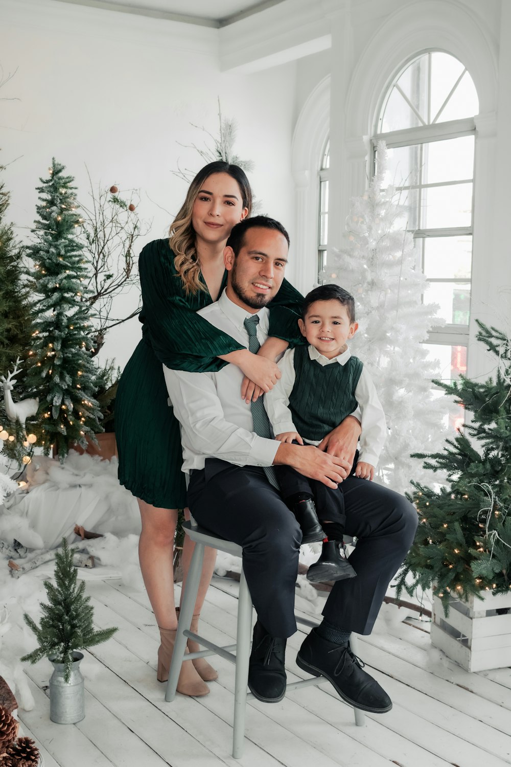 a man, woman and child sitting on a chair in front of a christmas tree