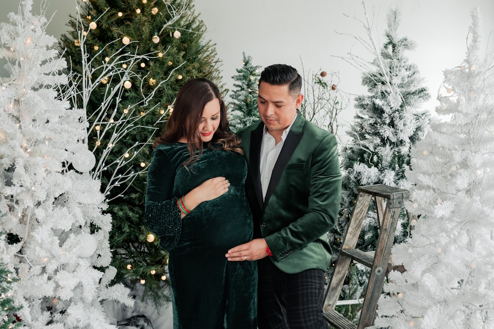 a pregnant couple standing in front of a christmas tree