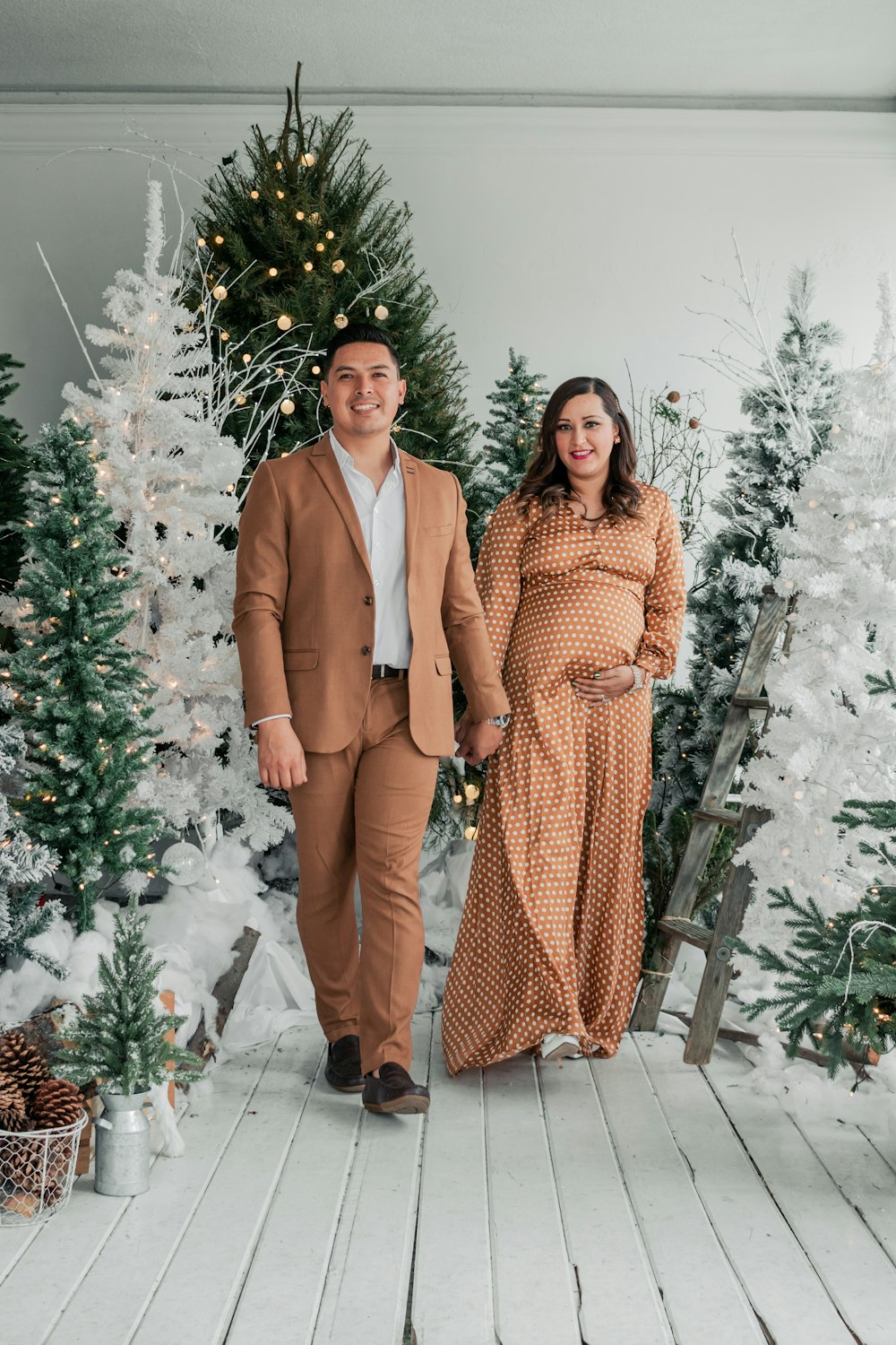 a pregnant couple standing in front of a christmas tree