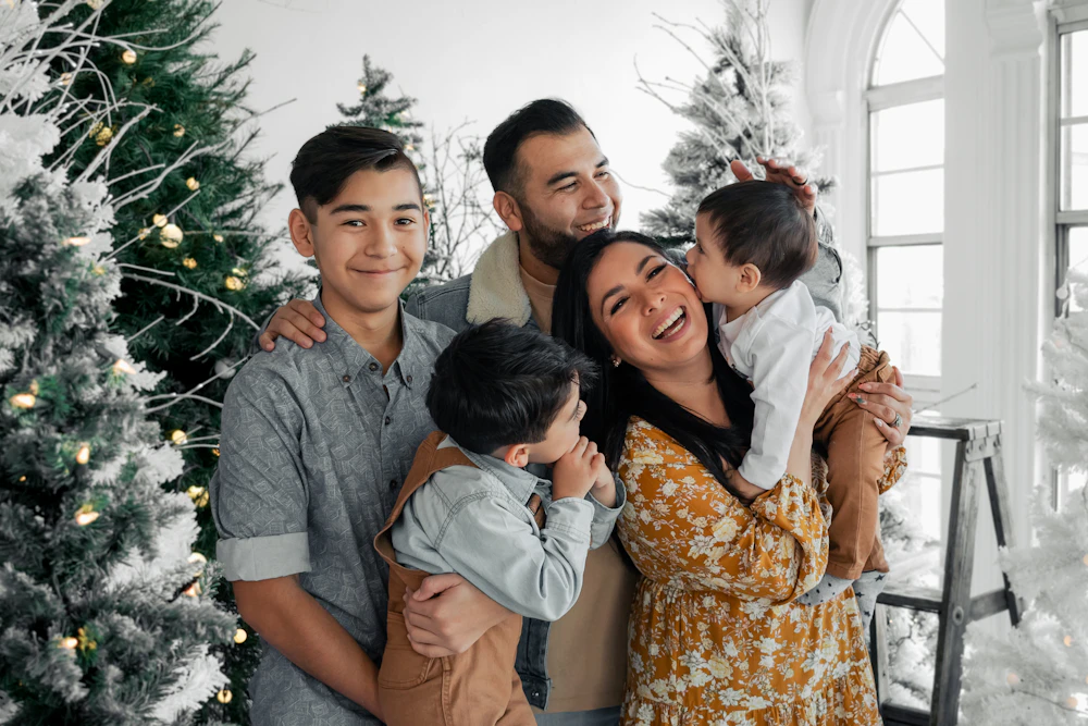 A smiling family of five posed in front of a white Christmas tree