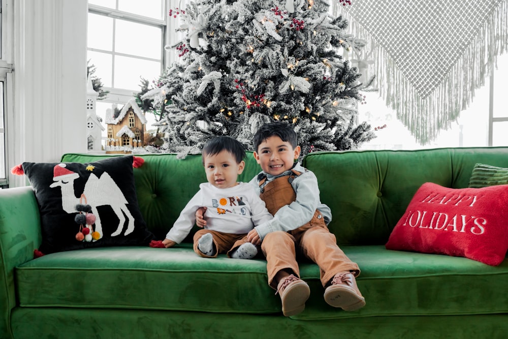 two children sitting on a green couch in front of a christmas tree