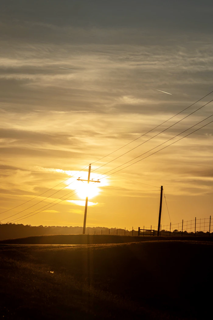 Soleil couchant sur un champ traversé par des lignes électriques