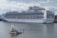 A large cruise ship docked at a port, displaying multiple decks and life rafts. The ship is white with blue accents and has the lettering 'Princess Cruises' on the side. In the foreground, an artistic glass structure floats on the water, resembling broken shards or ice.