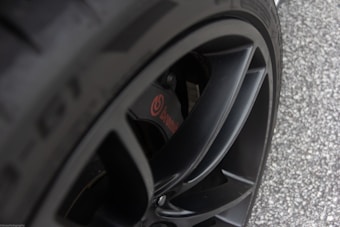 Close-up view of a black alloy wheel with a visible Brembo brake caliper. The tire's texture and detailed engraving can be seen, with a background of asphalt.