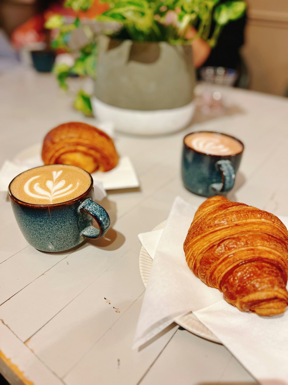 a table topped with two cups of coffee and a croissant