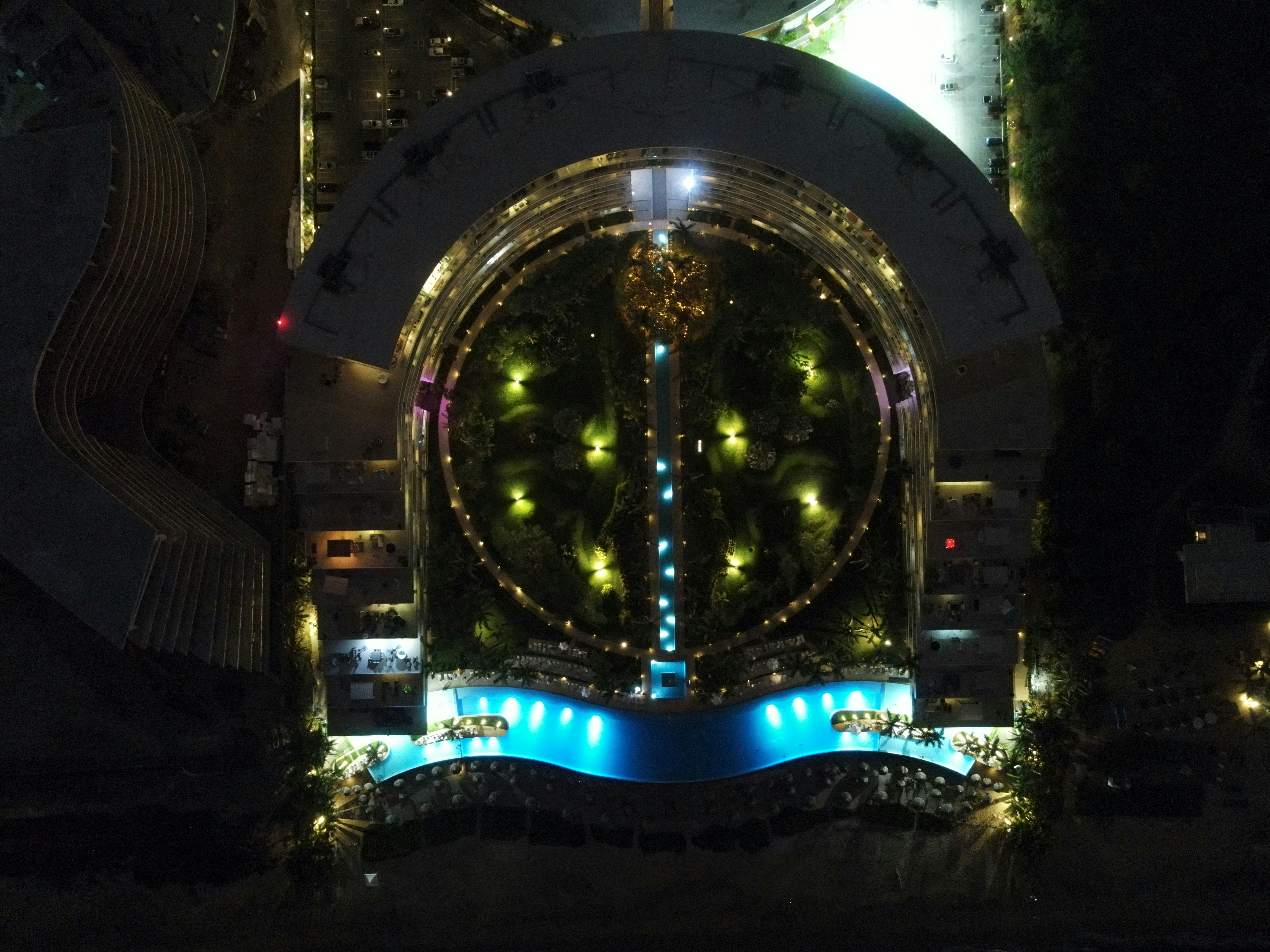 Aerial view of luxury infinity pool at night, deep shadows, warm accent lights, architectural luxury resort, dark atmospheric