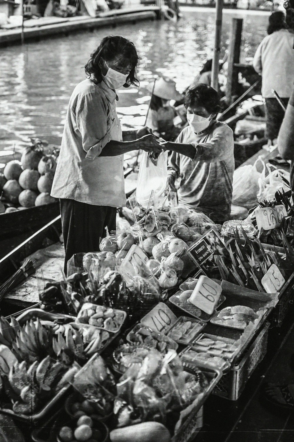 a black and white photo of people in a boat selling produce