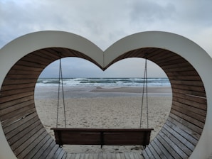 a heart shaped bench sitting on top of a sandy beach