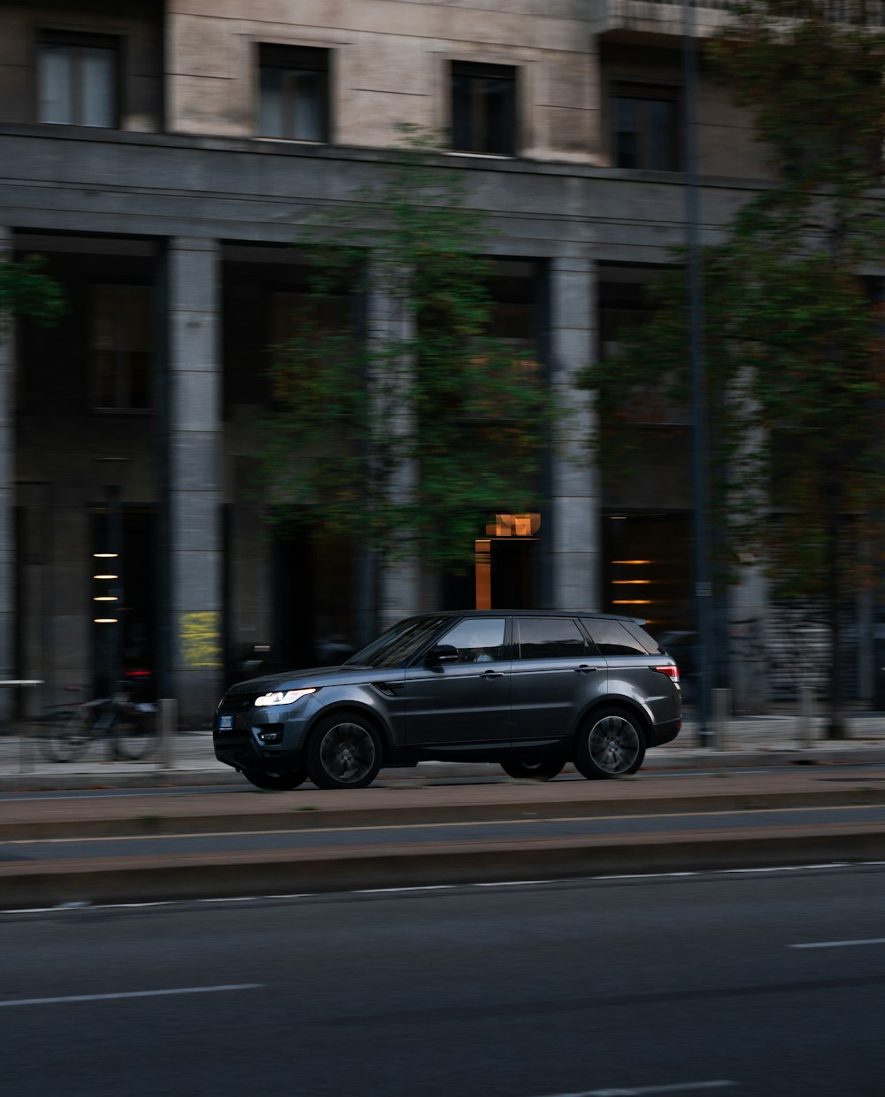 a black suv driving down a street next to a tall building