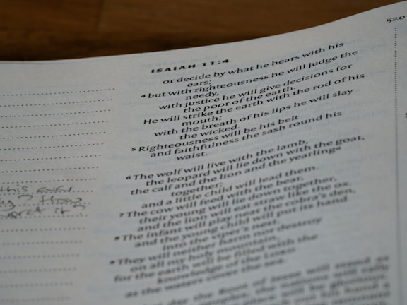 A close-up of a page from a book featuring text from the book of Isaiah. The passage includes verses and is printed in a traditional serif font. The text is black on a white background with a margin on the left including some handwritten notes.