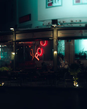Evening scene of the café’s exterior with subtle neon signage glowing against the dark theme.