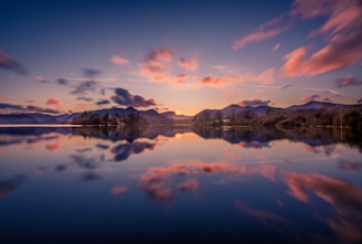 A tranquil lake reflecting a vibrant sunset with distant hills.