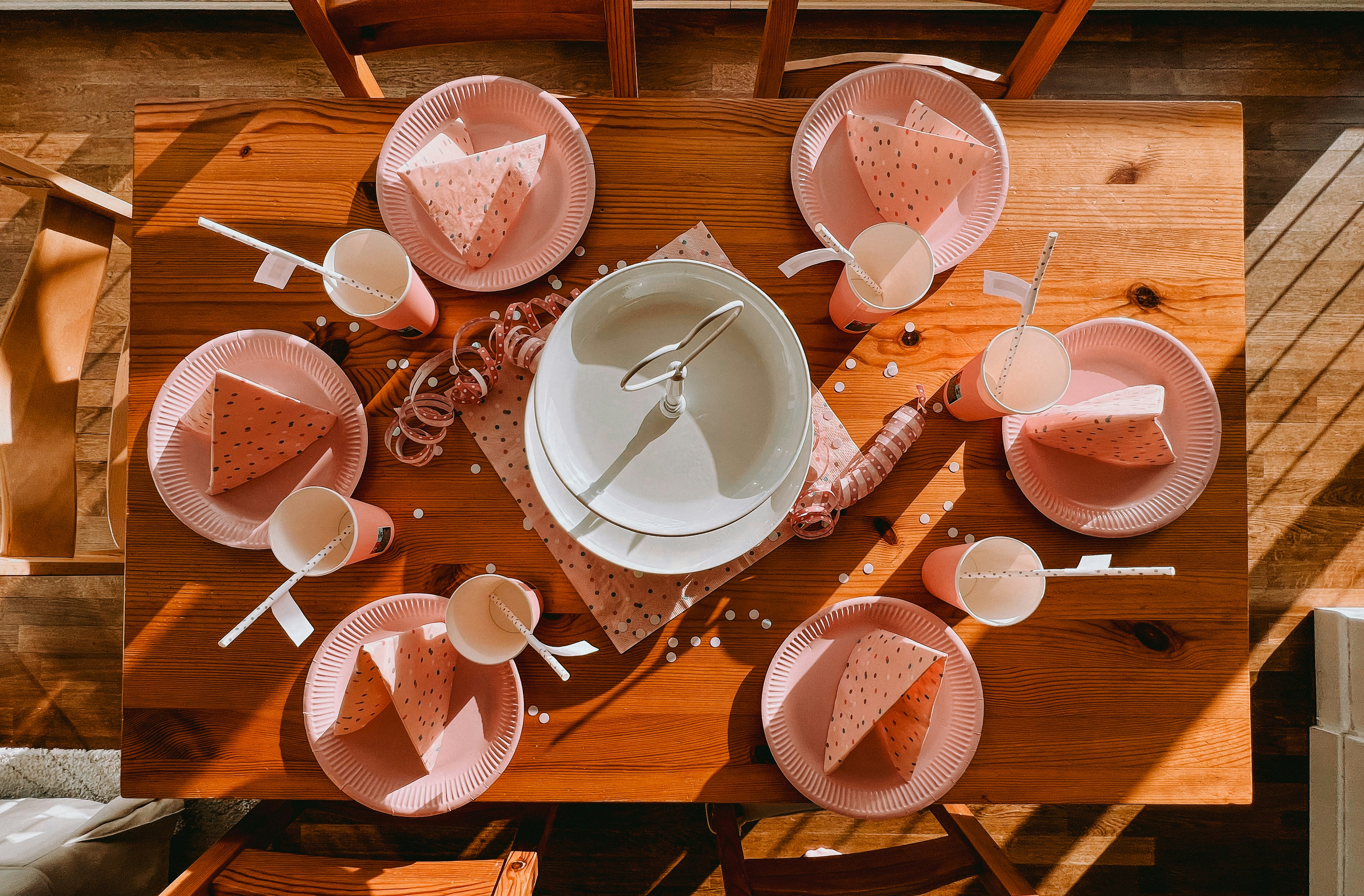 a wooden table topped with pink plates and cups