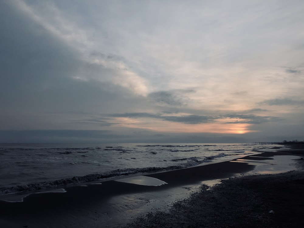 the sun is setting over the ocean on a cloudy day