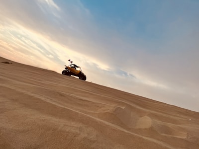 Sunset casting warm hues over rolling golden dunes as a 4x4 vehicle climbs a sandy hill.