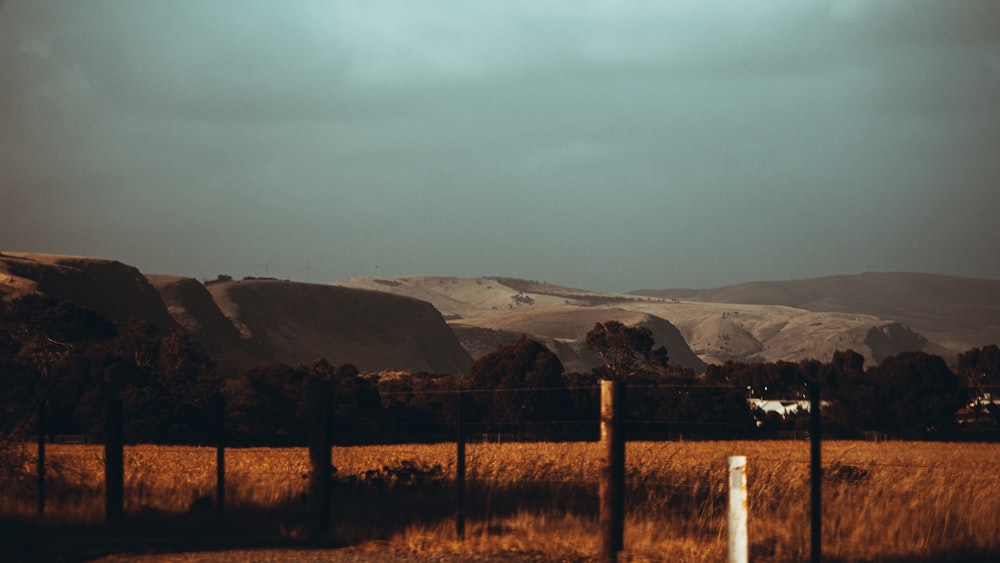 a field with a fence and mountains in the background