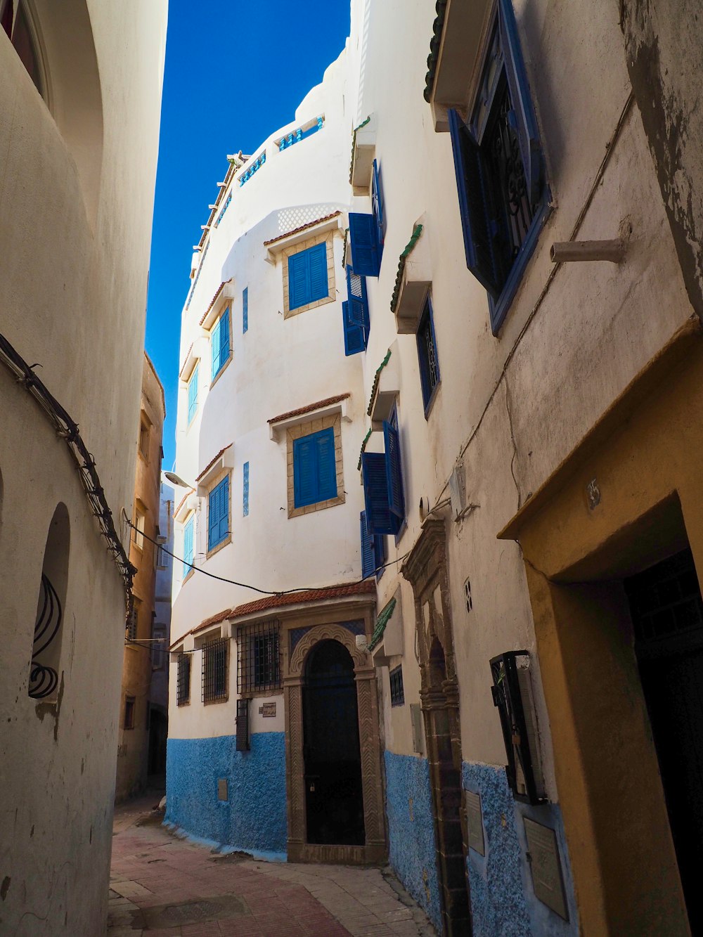 a narrow alley way with a white building and blue shutters