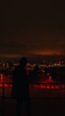 Silhouetted figure against a foggy cityscape at night, bathed in deep red hues.