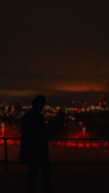 A silhouette of a tall figure blending into a bustling city crowd under a twilight sky.