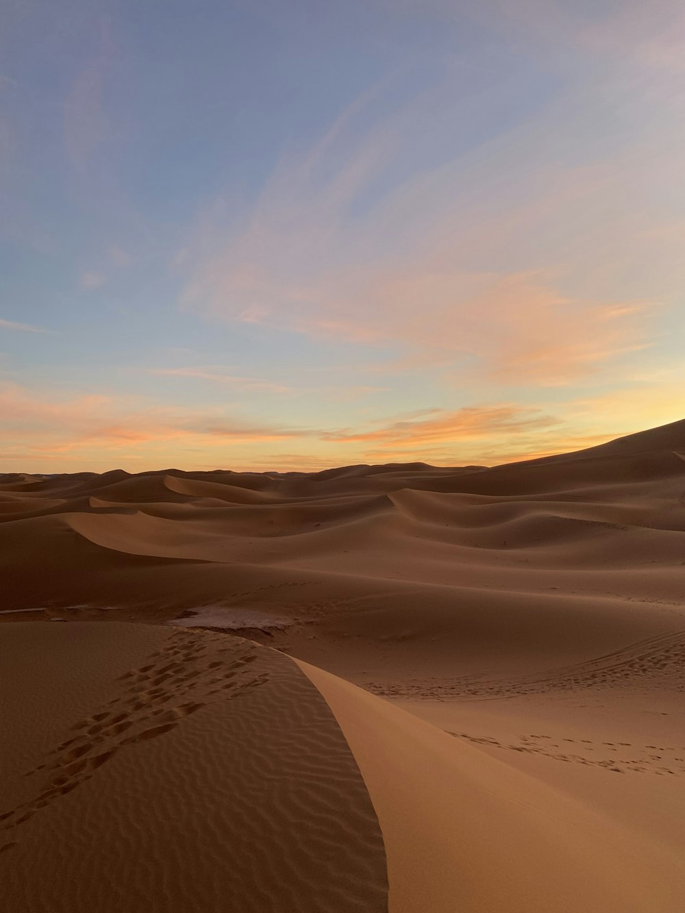 a sunset in the desert with footprints in the sand