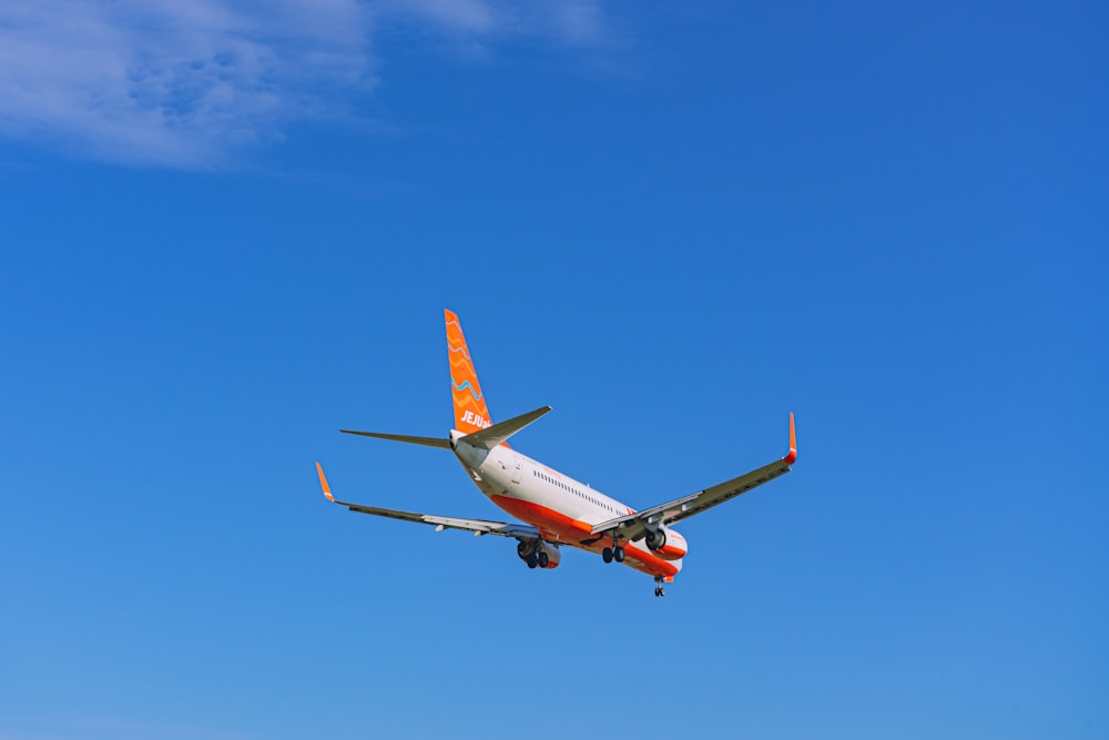 an orange and white airplane flying in a blue sky