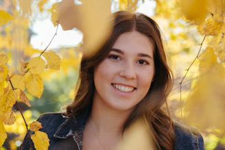 A sunlit outdoor portrait of a woman laughing amidst autumn leaves.