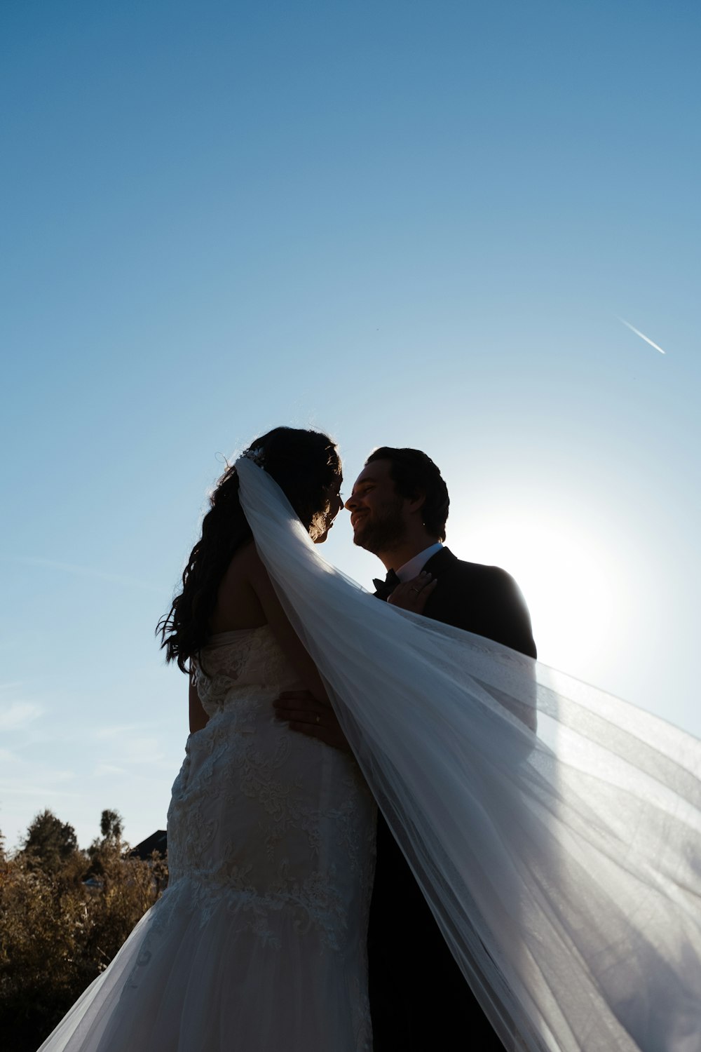 a bride and groom kissing in front of the sun
