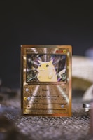 A shiny collectible card featuring a yellow fictional creature with pointed ears and a friendly expression. The card has a golden border and displays various statistics and attack details. The background is slightly blurred, emphasizing the card in the foreground.