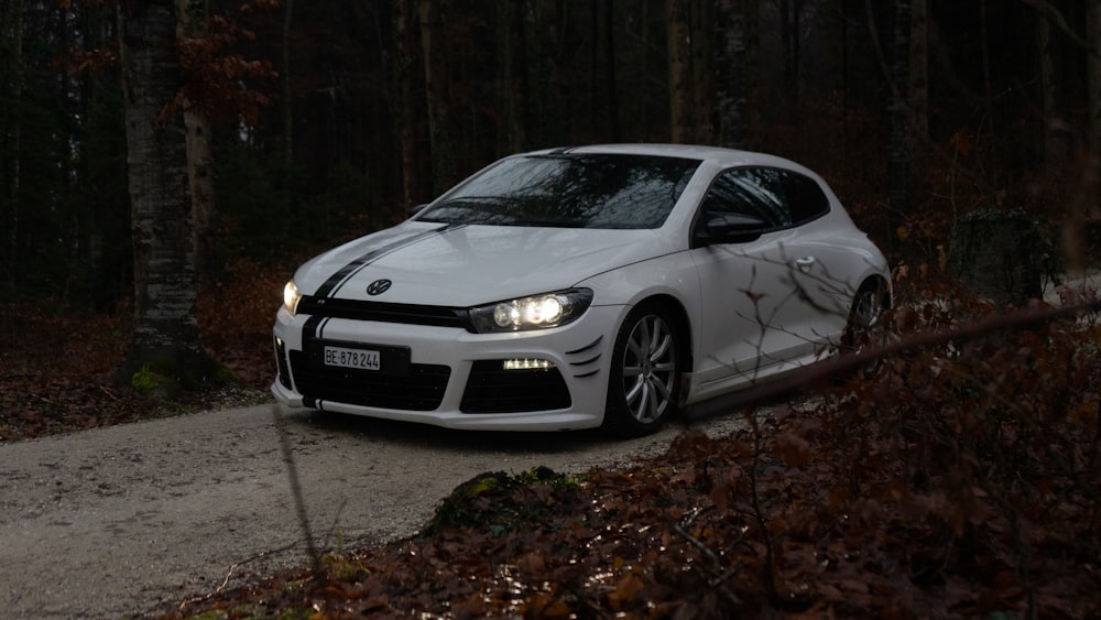 a white car driving down a dirt road in the woods