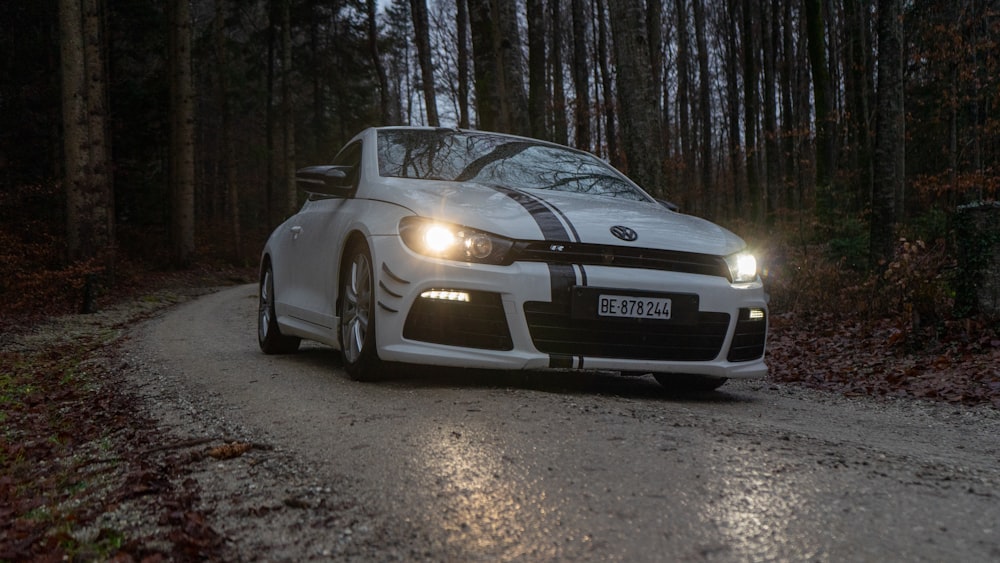 a white sports car driving down a forest road