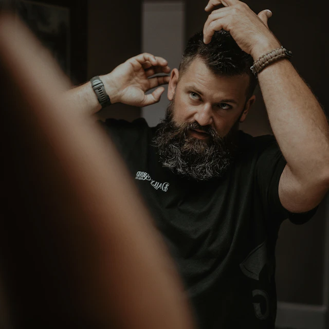 A man with a goatee combing pomade through his hair