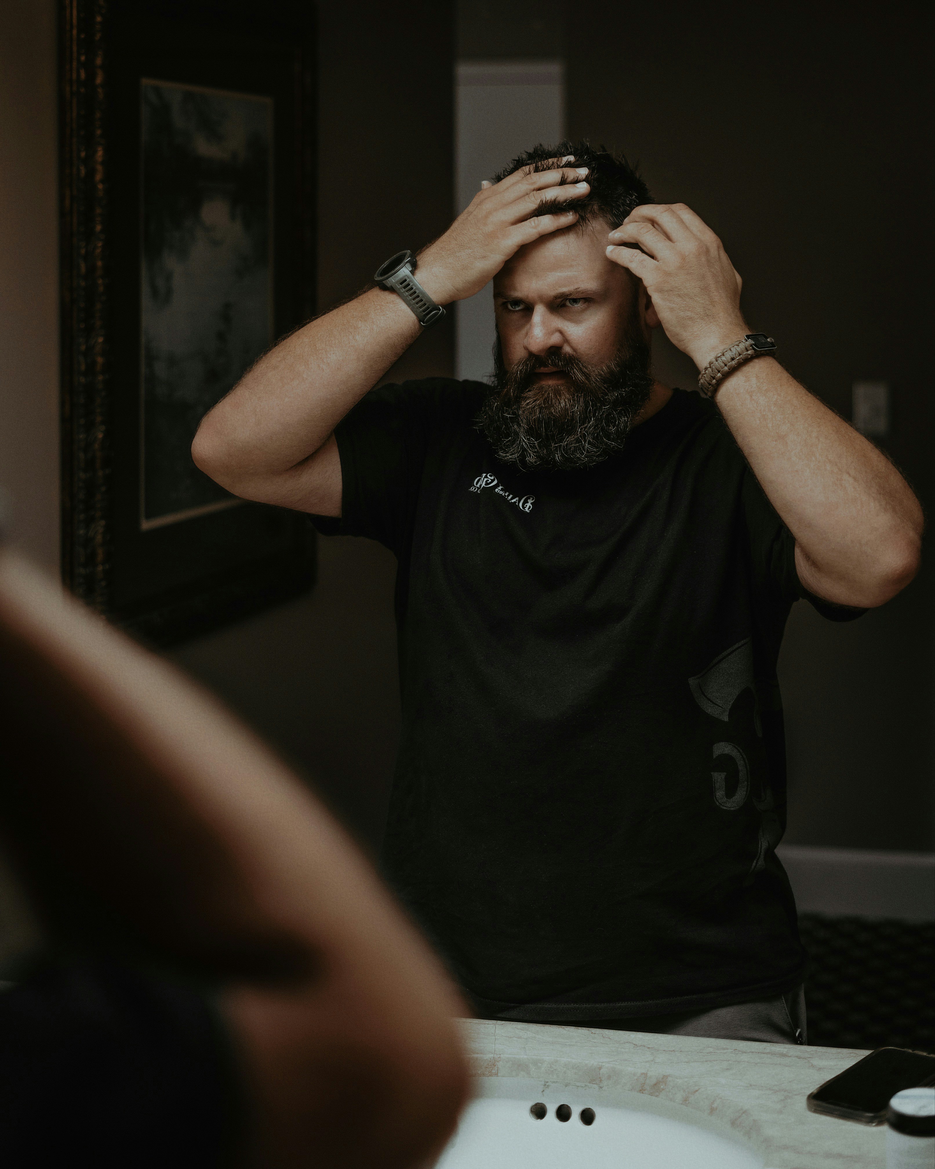 Candid photo of a bearded man applying Daily Grind pomade to his hair. Photo by Lance Reis / KickassDesigns on IG