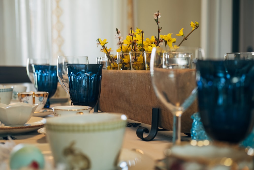 a table set with blue glassware and yellow flowers