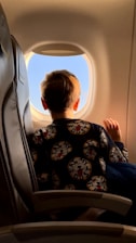 a little boy sitting in an airplane seat looking out the window